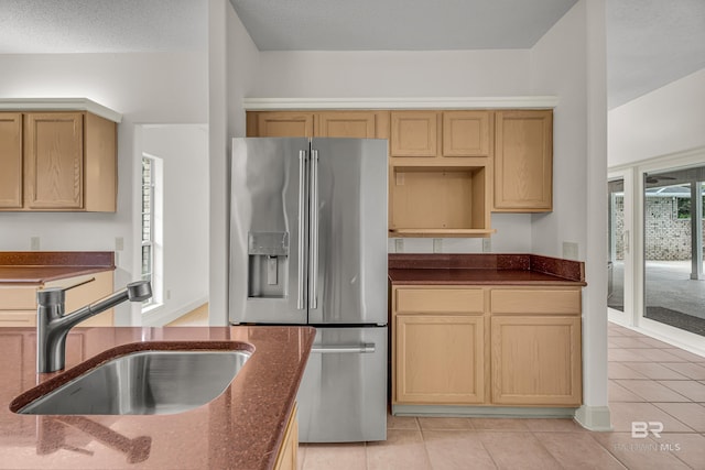 kitchen with stainless steel fridge, a sink, dark stone counters, and light tile patterned floors