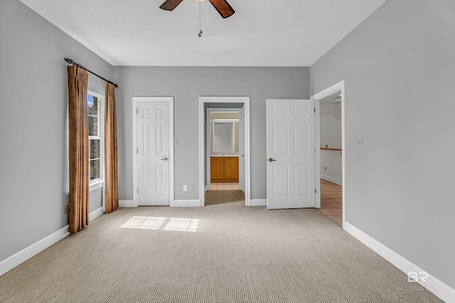 unfurnished bedroom featuring baseboards, ceiling fan, ensuite bath, and light carpet