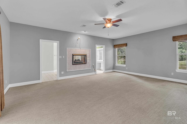 unfurnished living room with carpet floors, a tiled fireplace, a ceiling fan, baseboards, and visible vents
