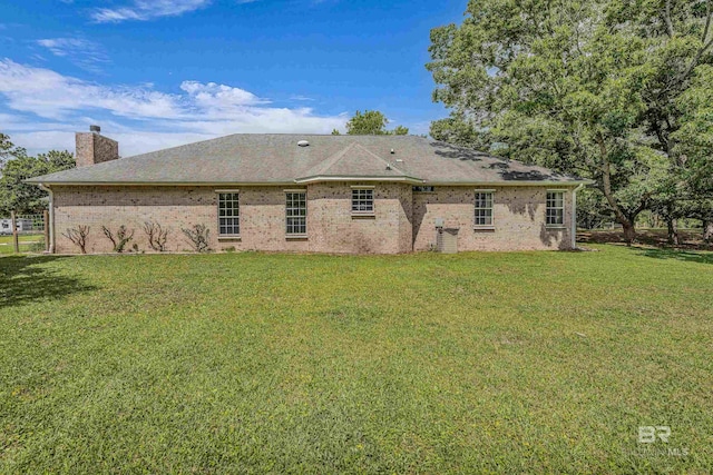 back of property featuring a yard, brick siding, and a chimney