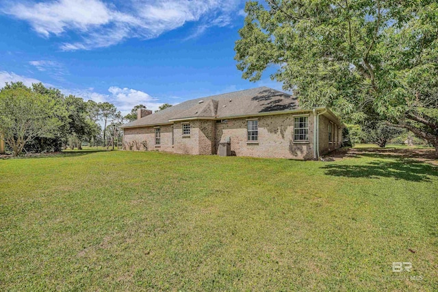 back of property featuring a lawn, a chimney, and brick siding