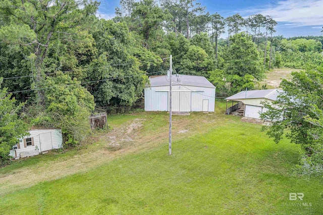 view of yard featuring an outdoor structure, a garage, a forest view, and a pole building