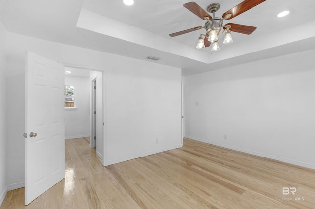 spare room with ceiling fan, a raised ceiling, and light hardwood / wood-style flooring