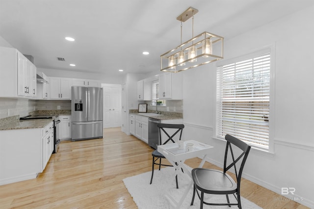 kitchen with sink, appliances with stainless steel finishes, white cabinetry, hanging light fixtures, and light hardwood / wood-style floors