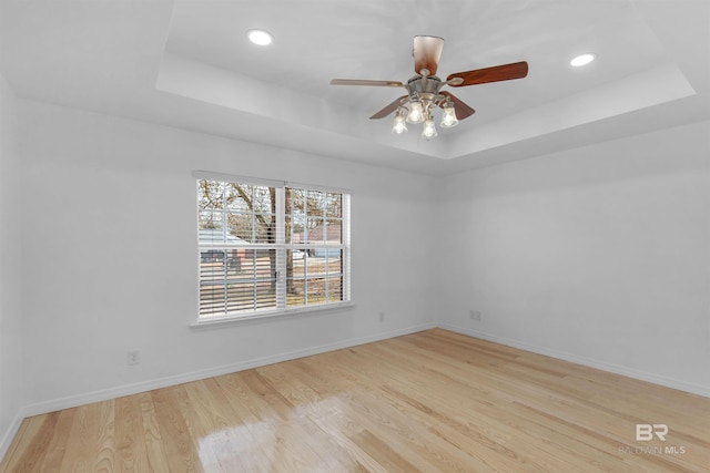 unfurnished room featuring a raised ceiling, ceiling fan, and light wood-type flooring