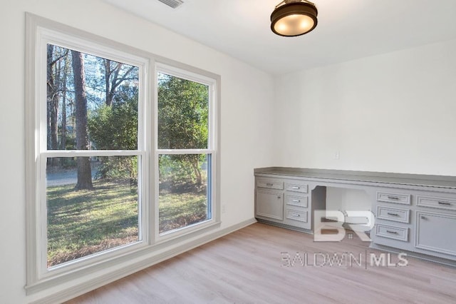 unfurnished office featuring baseboards, built in study area, a wealth of natural light, and light wood-style floors