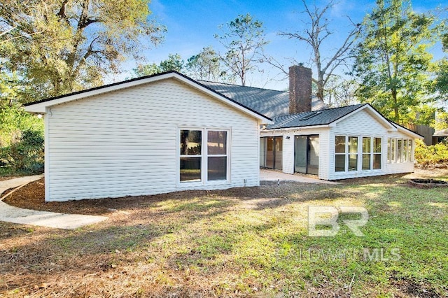 back of property with a chimney and a lawn