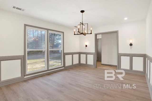 unfurnished dining area with light wood-style floors, wainscoting, visible vents, and a decorative wall