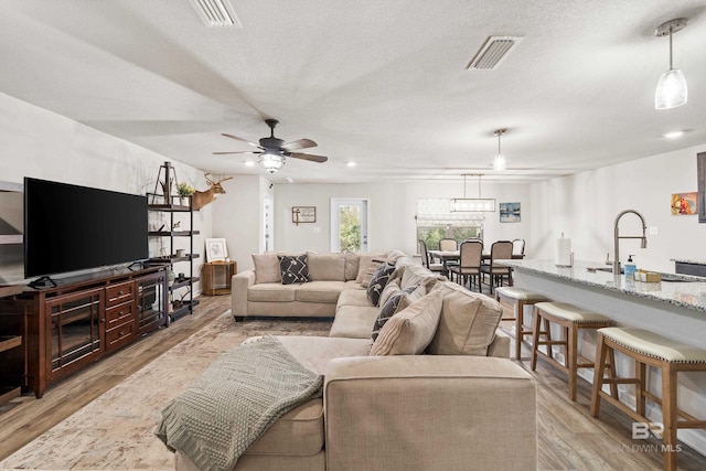 living room with ceiling fan, sink, light hardwood / wood-style floors, and a textured ceiling