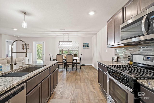 kitchen with sink, decorative light fixtures, light stone counters, dark brown cabinetry, and stainless steel appliances