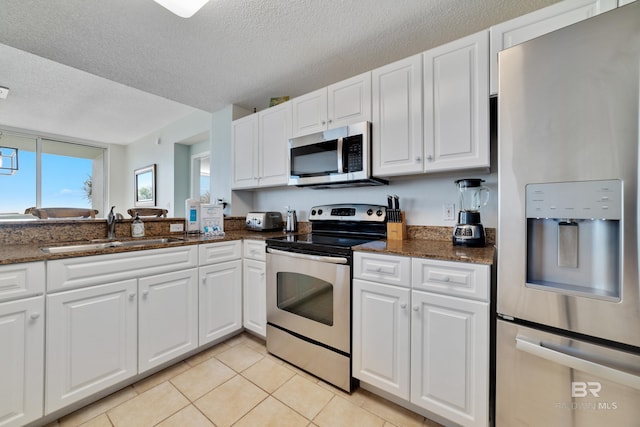 kitchen with a sink, stainless steel appliances, light tile patterned floors, and white cabinetry