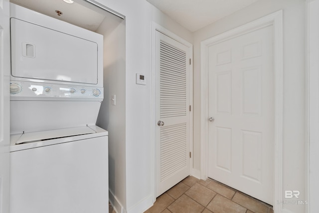 clothes washing area with light tile patterned floors, laundry area, stacked washer / drying machine, and baseboards