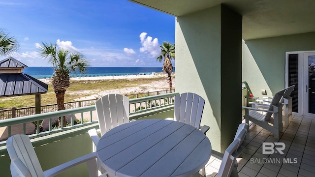 balcony with outdoor dining area, a view of the beach, and a water view