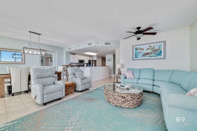 living area with light tile patterned floors, visible vents, a textured ceiling, and a ceiling fan