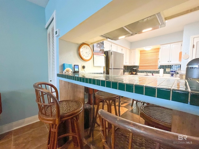 kitchen featuring stainless steel refrigerator, dark tile patterned flooring, decorative backsplash, white cabinets, and tile countertops