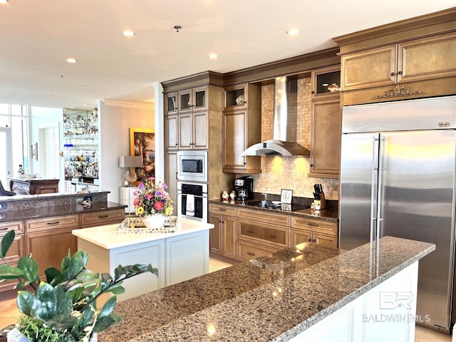 kitchen featuring dark stone counters, a center island, backsplash, wall chimney exhaust hood, and built in appliances