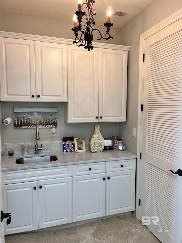 kitchen featuring light tile patterned floors, white cabinetry, light stone countertops, and sink