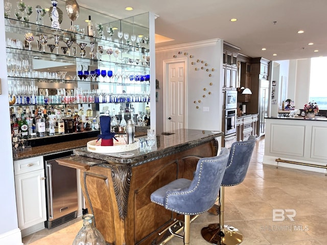 bar with dark stone counters, light tile patterned floors, crown molding, and stainless steel appliances