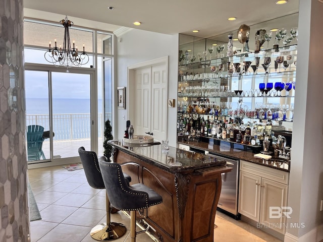 bar featuring dark stone counters, a water view, light tile patterned floors, and stainless steel dishwasher