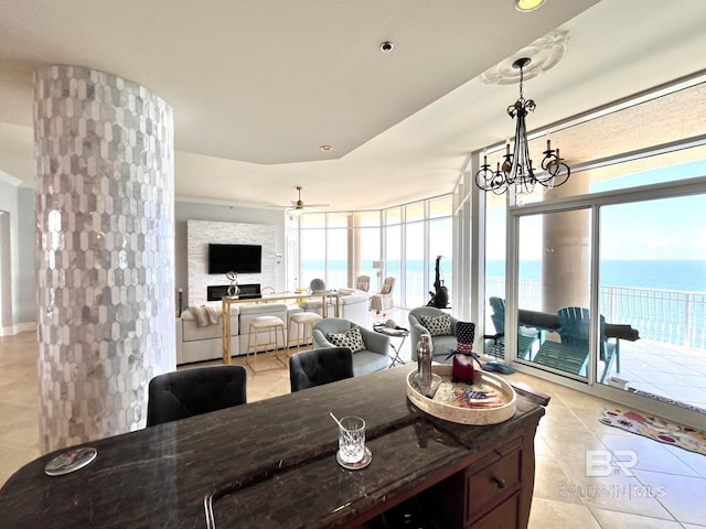 dining space with a large fireplace, a wall of windows, ceiling fan with notable chandelier, and light tile patterned floors