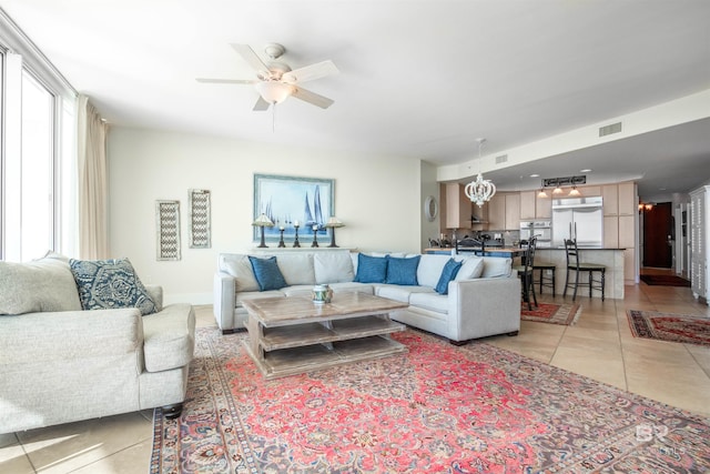 tiled living room with ceiling fan with notable chandelier and plenty of natural light