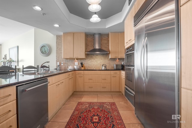 kitchen with light brown cabinets, wall chimney exhaust hood, light tile patterned floors, a tray ceiling, and stainless steel appliances