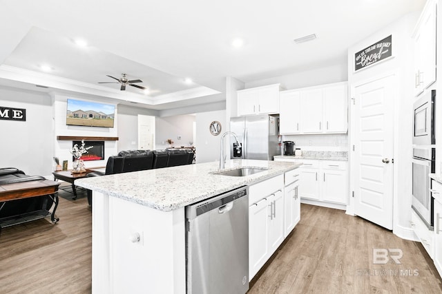 kitchen with appliances with stainless steel finishes, white cabinetry, an island with sink, sink, and a tray ceiling