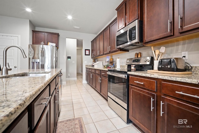 kitchen with light stone counters, light tile patterned floors, appliances with stainless steel finishes, and sink