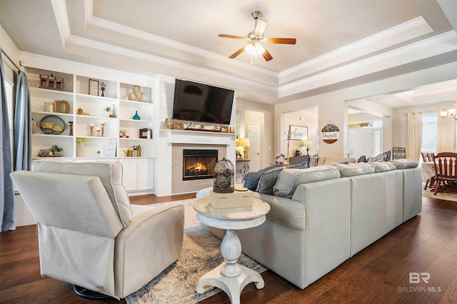 living room with ceiling fan with notable chandelier, a tray ceiling, a fireplace, and dark hardwood / wood-style flooring