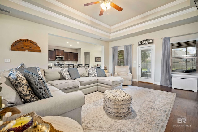 living room with ceiling fan, a raised ceiling, dark wood-type flooring, and crown molding