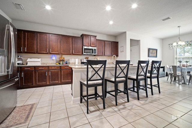 kitchen featuring light stone counters, hanging light fixtures, an inviting chandelier, a center island with sink, and appliances with stainless steel finishes