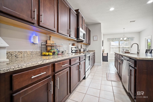 kitchen featuring light stone counters, sink, decorative light fixtures, stainless steel appliances, and an inviting chandelier