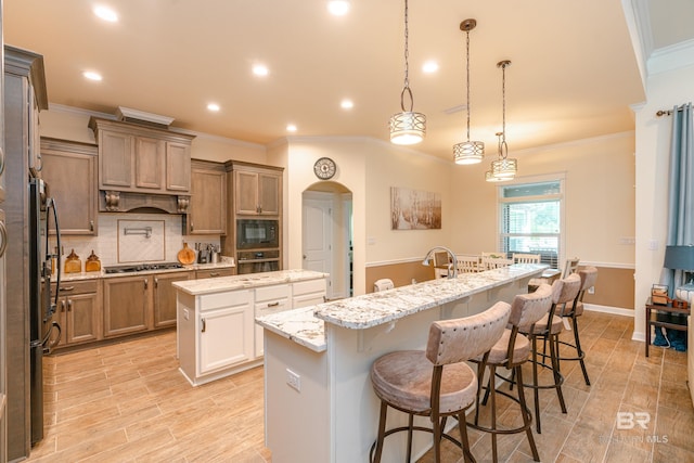 kitchen with a center island with sink, black appliances, decorative light fixtures, tasteful backsplash, and a kitchen bar