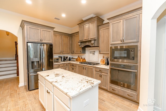 kitchen featuring a kitchen island, backsplash, light stone countertops, ornamental molding, and appliances with stainless steel finishes