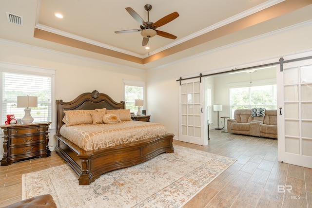 bedroom with a barn door, a tray ceiling, crown molding, and ceiling fan