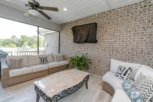 living room with brick wall, wood-type flooring, and ceiling fan