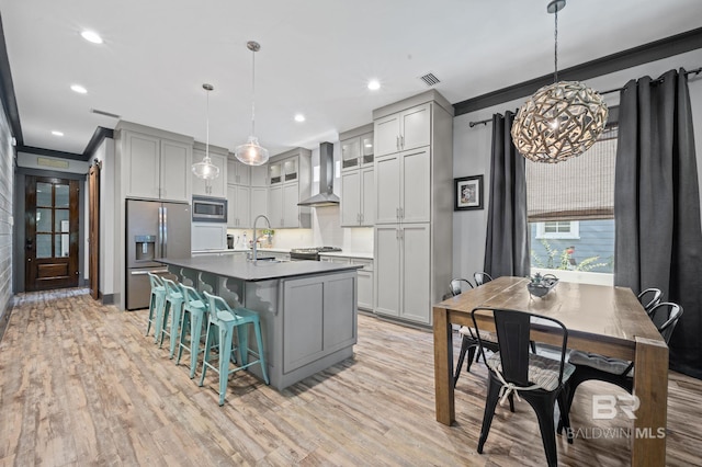 kitchen with wall chimney range hood, ornamental molding, light wood-type flooring, stainless steel appliances, and pendant lighting