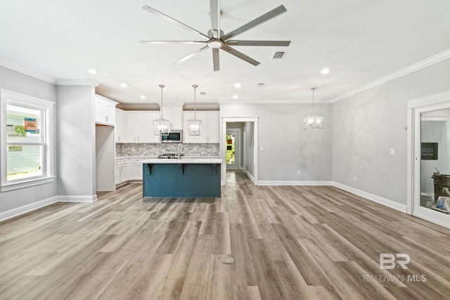 kitchen featuring pendant lighting, decorative backsplash, a kitchen island, ornamental molding, and light hardwood / wood-style flooring