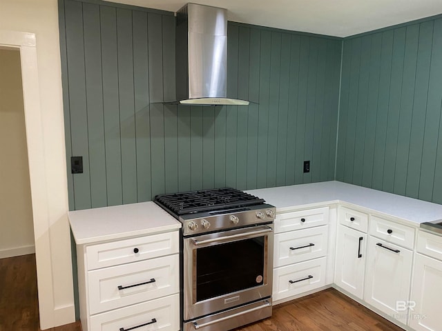 kitchen with hardwood / wood-style floors, stainless steel gas range oven, wall chimney exhaust hood, white cabinets, and wooden walls