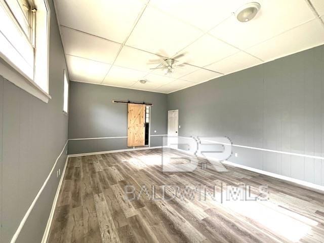 unfurnished room with hardwood / wood-style flooring, a barn door, a paneled ceiling, and ceiling fan