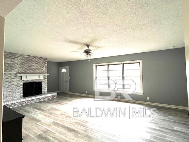 unfurnished living room with ceiling fan, a fireplace, hardwood / wood-style floors, and a textured ceiling