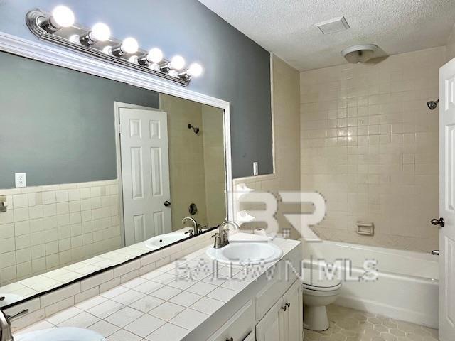 full bathroom featuring vanity, a textured ceiling, tile patterned floors, toilet, and tiled shower / bath