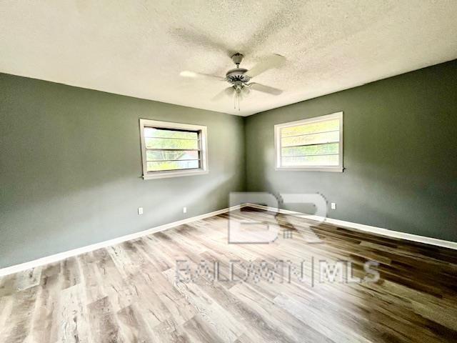 empty room featuring ceiling fan, a healthy amount of sunlight, a textured ceiling, and light wood-type flooring