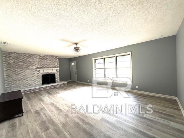 unfurnished living room with ceiling fan, hardwood / wood-style flooring, a fireplace, and a textured ceiling