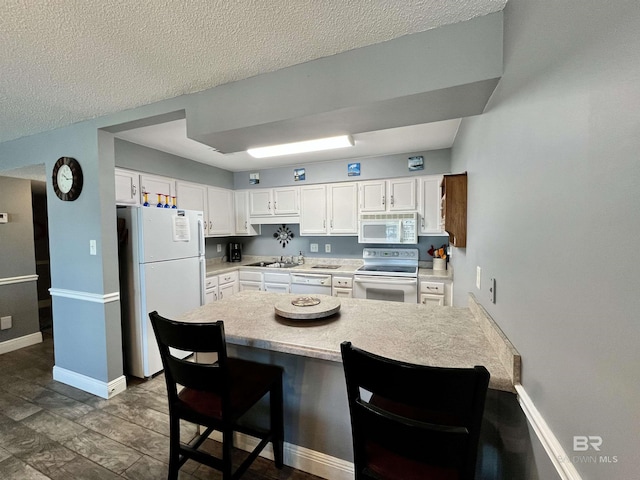 kitchen featuring sink, white cabinetry, a kitchen breakfast bar, kitchen peninsula, and white appliances