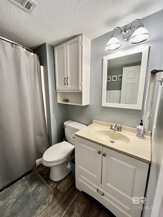 bathroom featuring wood-type flooring, vanity, walk in shower, toilet, and a textured ceiling