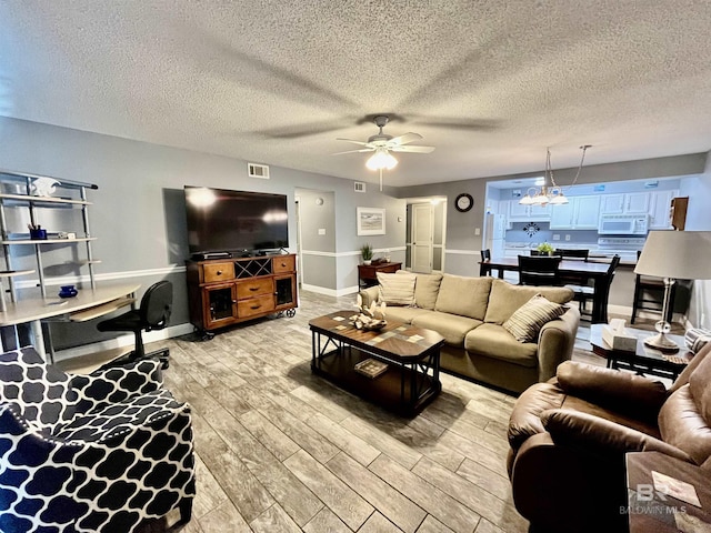 living room featuring ceiling fan with notable chandelier, light hardwood / wood-style flooring, and a textured ceiling