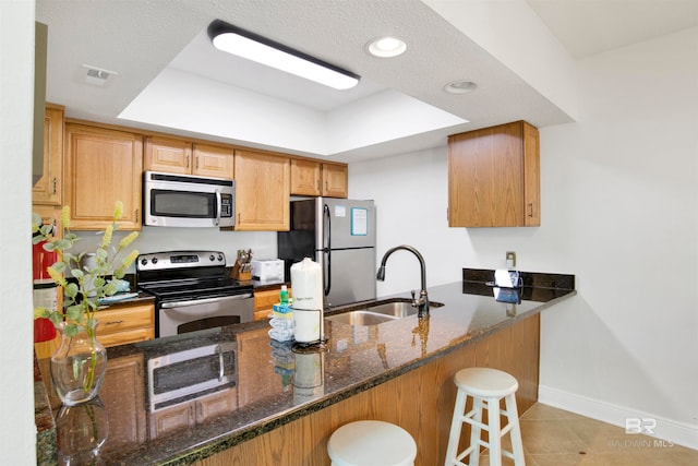 kitchen featuring sink, kitchen peninsula, stainless steel appliances, a breakfast bar, and dark stone countertops