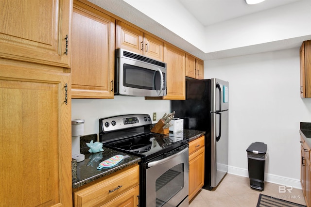 kitchen featuring appliances with stainless steel finishes, dark stone counters, and light tile patterned floors