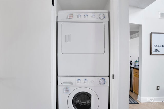 laundry area featuring stacked washer / drying machine and light tile patterned flooring